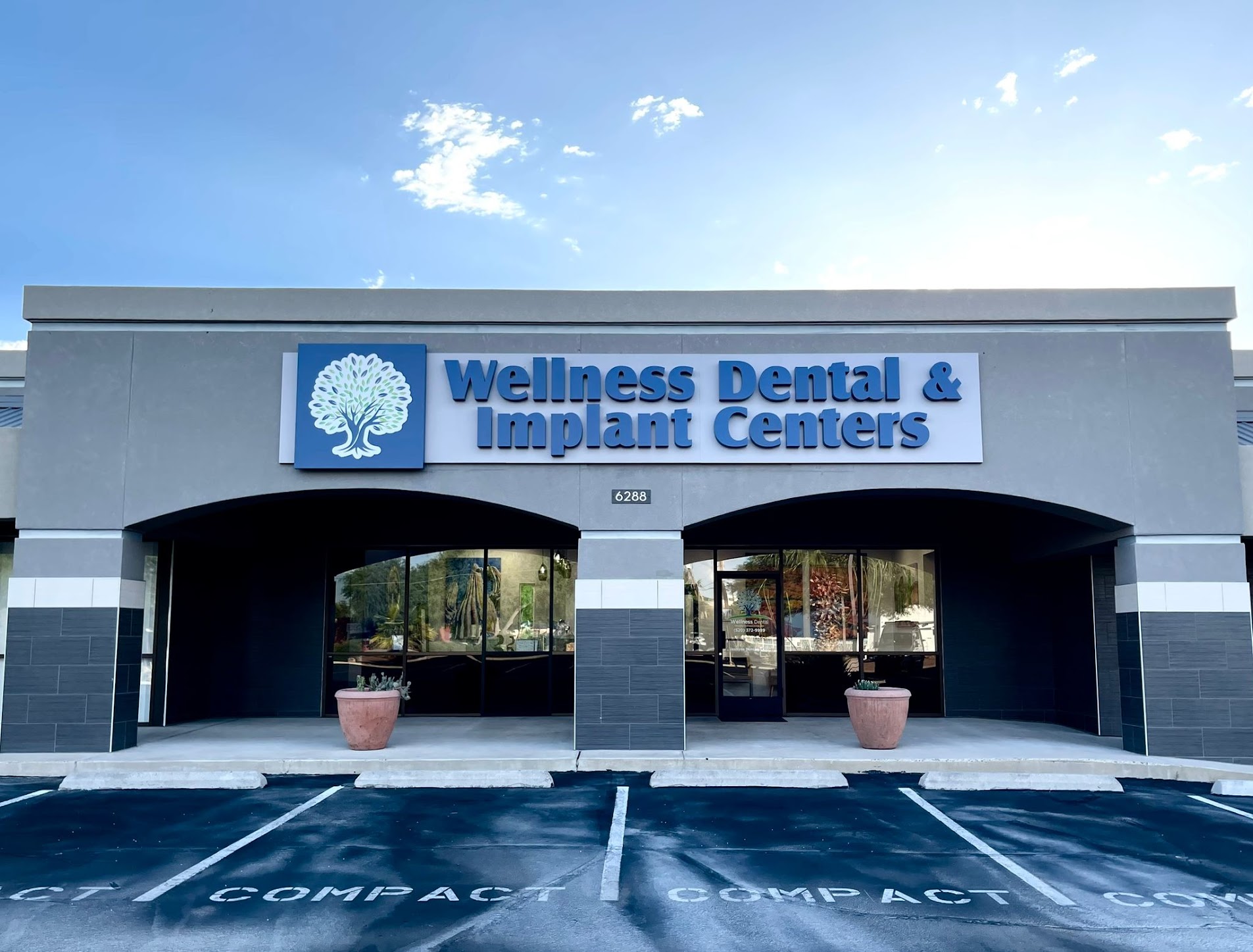 The Wellness Dental & Implant Centers storefront on E Grant Rd, Tucson, seen head-on from the parking bays directly outside the entrance.