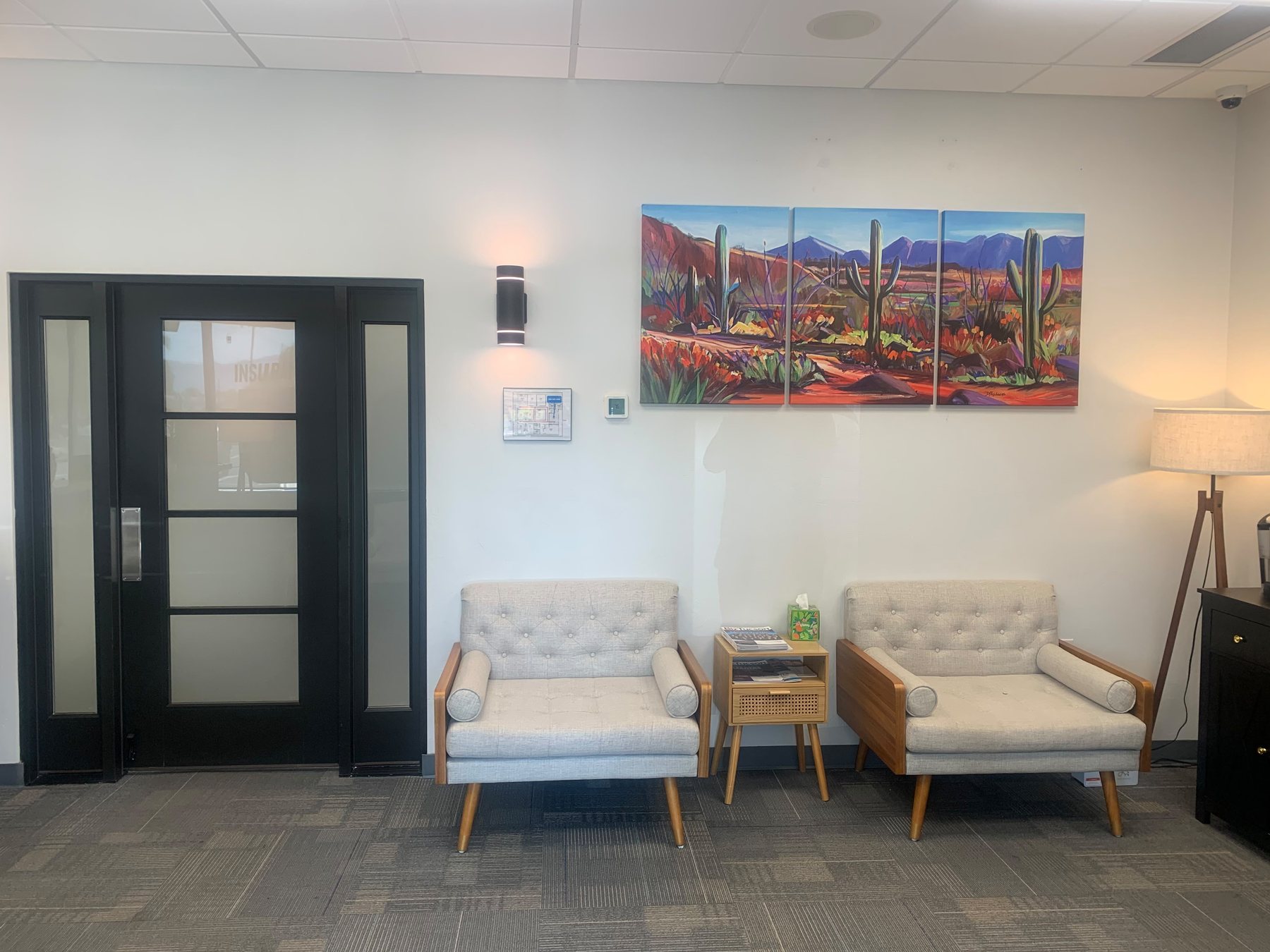 The entrance to the waiting area, with armchairs and a desert landscape triptych